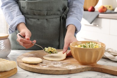 Photo of Woman making pirozhki (stuffed pastry pies) with eggs and dill at white marble table indoors, closeup