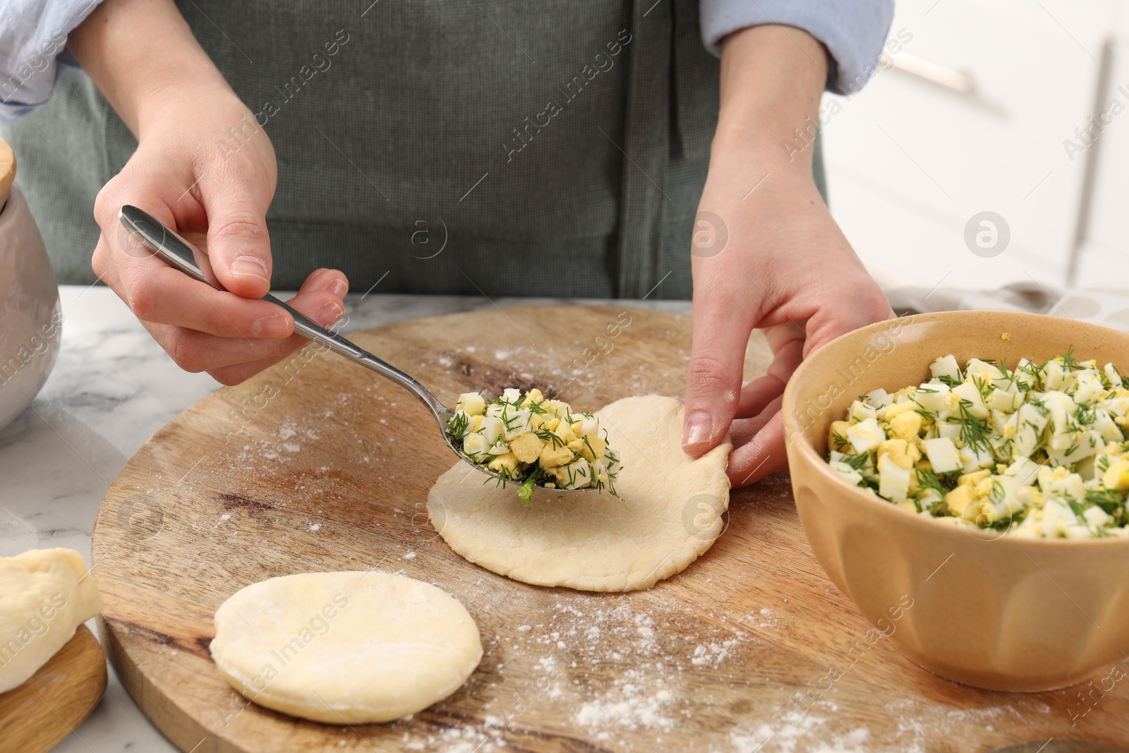 Photo of Woman making pirozhki (stuffed pastry pies) with eggs and dill at table indoors, closeup