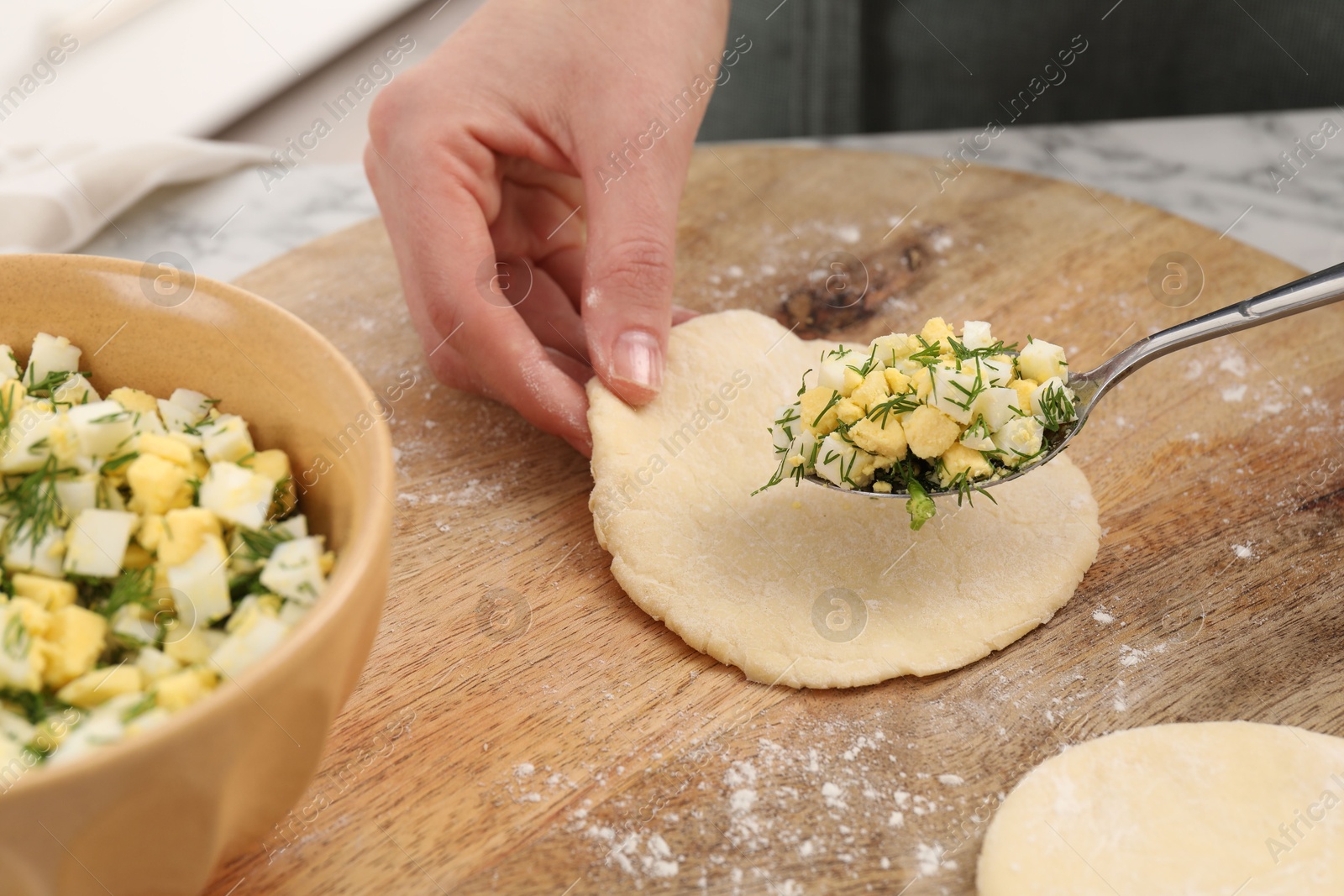 Photo of Woman making pirozhki (stuffed pastry pies) with eggs and dill at table indoors, closeup