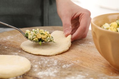 Photo of Woman making pirozhki (stuffed pastry pies) with eggs and dill at table, closeup