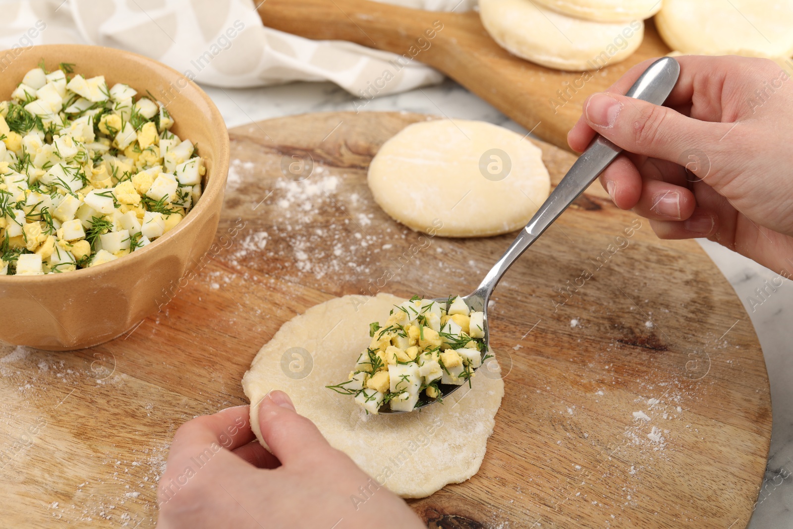 Photo of Woman making pirozhki (stuffed pastry pies) with eggs and dill at table, closeup