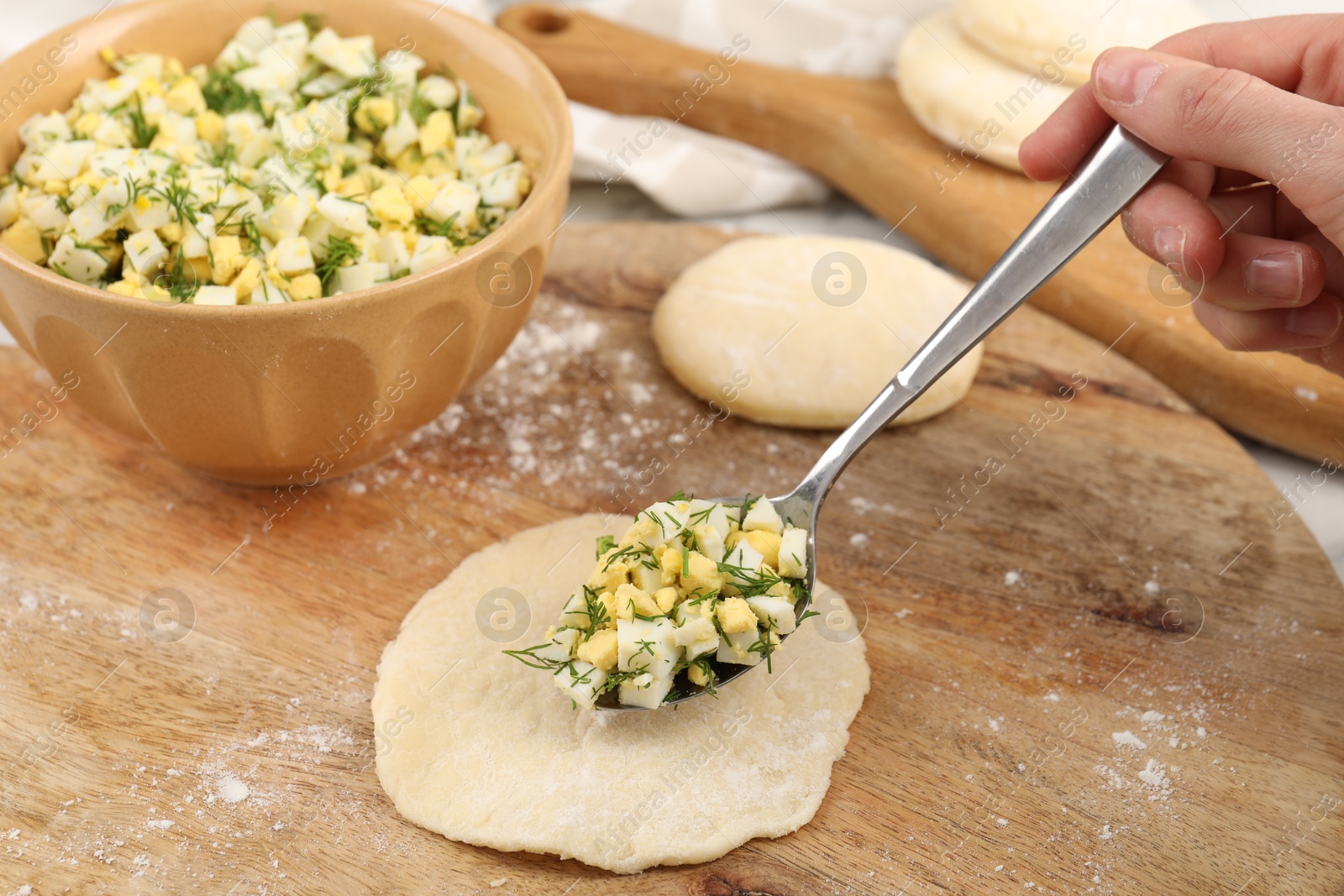 Photo of Woman making pirozhki (stuffed pastry pies) with eggs and dill at table, closeup