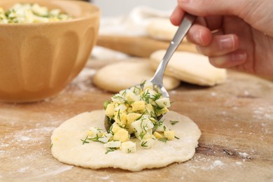 Photo of Woman making pirozhki (stuffed pastry pies) with eggs and dill at table, closeup