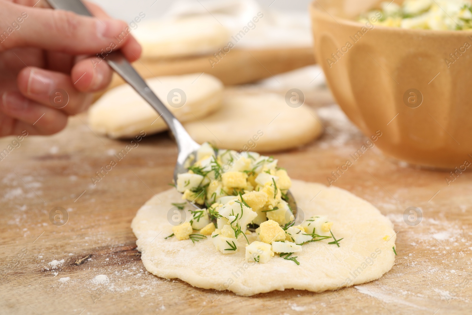 Photo of Woman making pirozhki (stuffed pastry pies) with eggs and dill at table, closeup