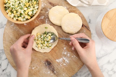 Photo of Woman making pirozhki (stuffed pastry pies) with eggs and dill at white table, top view