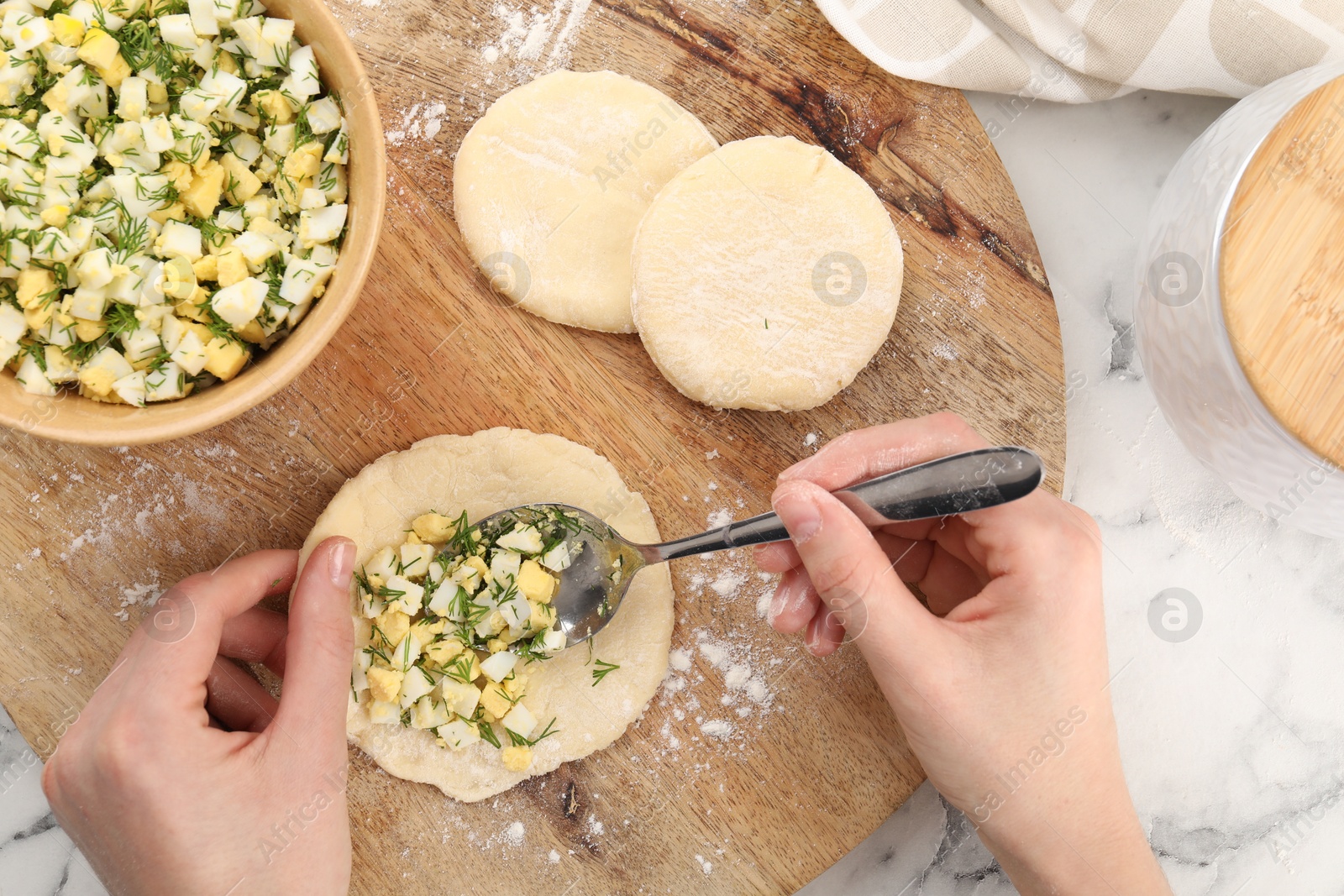 Photo of Woman making pirozhki (stuffed pastry pies) with eggs and dill at white table, top view