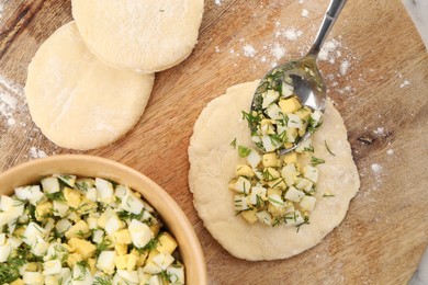 Photo of Making pirozhki (stuffed pastry pies). Pieces of dough with eggs and dill filling on table, flat lay