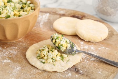 Photo of Making pirozhki (stuffed pastry pies). Pieces of dough with eggs and dill filling on table, closeup