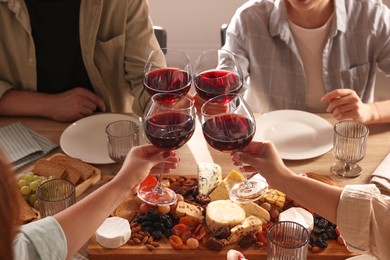 Photo of People clinking glasses of red wine at served table, closeup