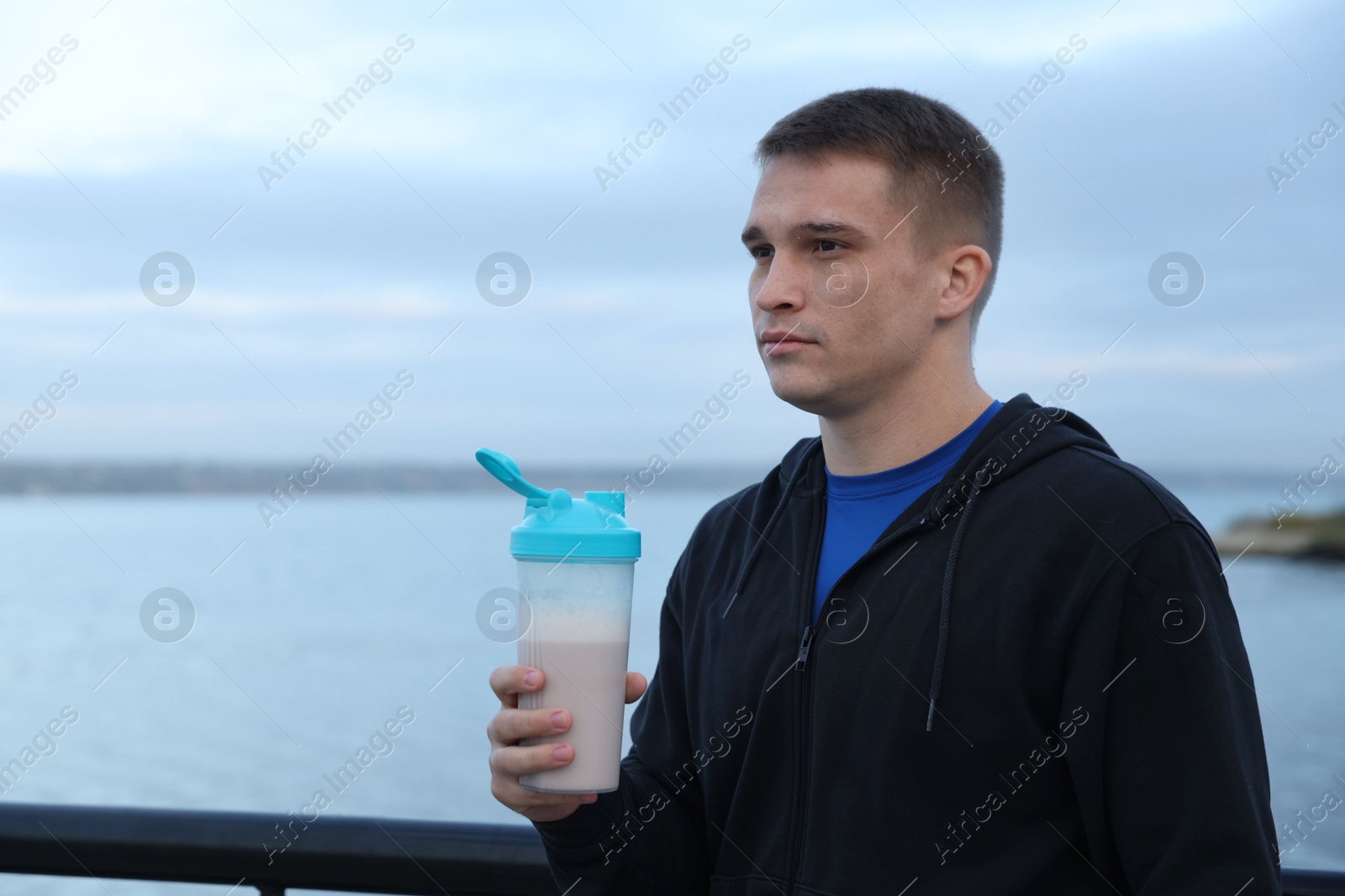 Photo of Athletic man with shaker of protein drink outdoors. Space for text