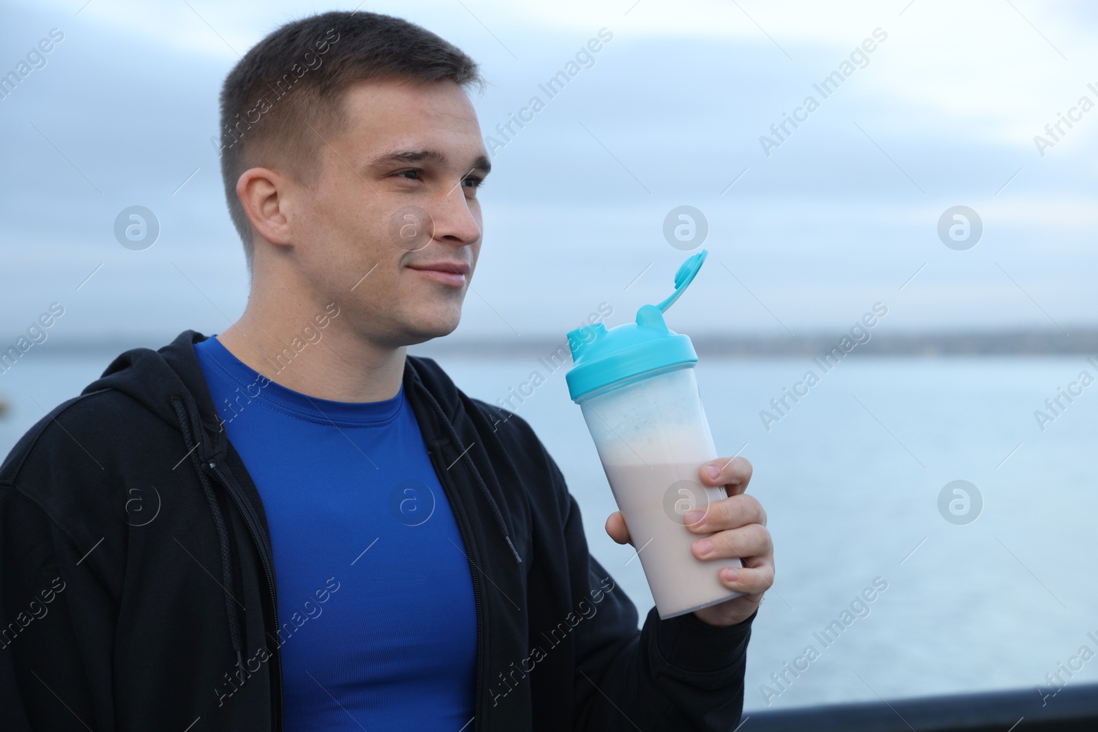 Photo of Athletic man with shaker of protein drink outdoors. Space for text