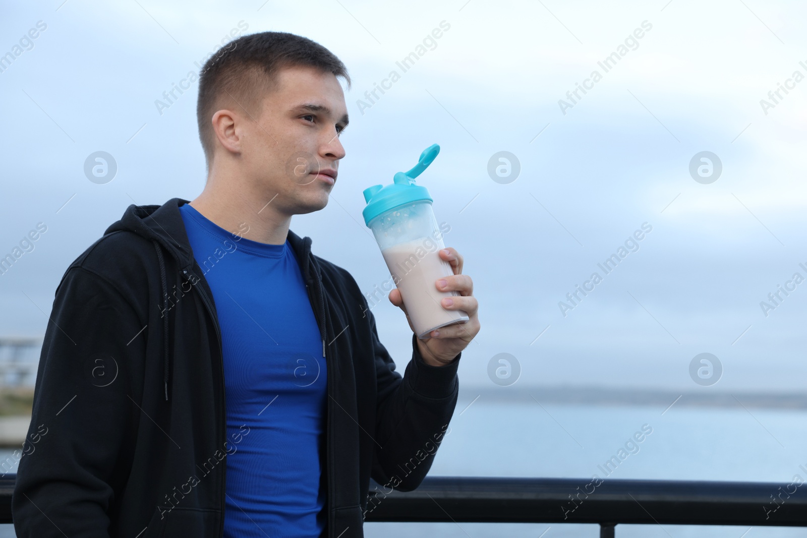 Photo of Athletic man with shaker of protein drink outdoors. Space for text