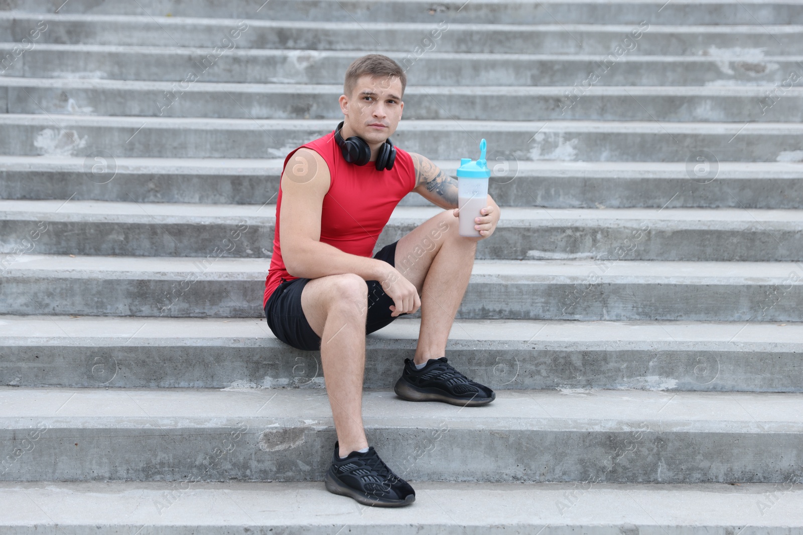 Photo of Athletic man with shaker of protein drink sitting on stairs outdoors