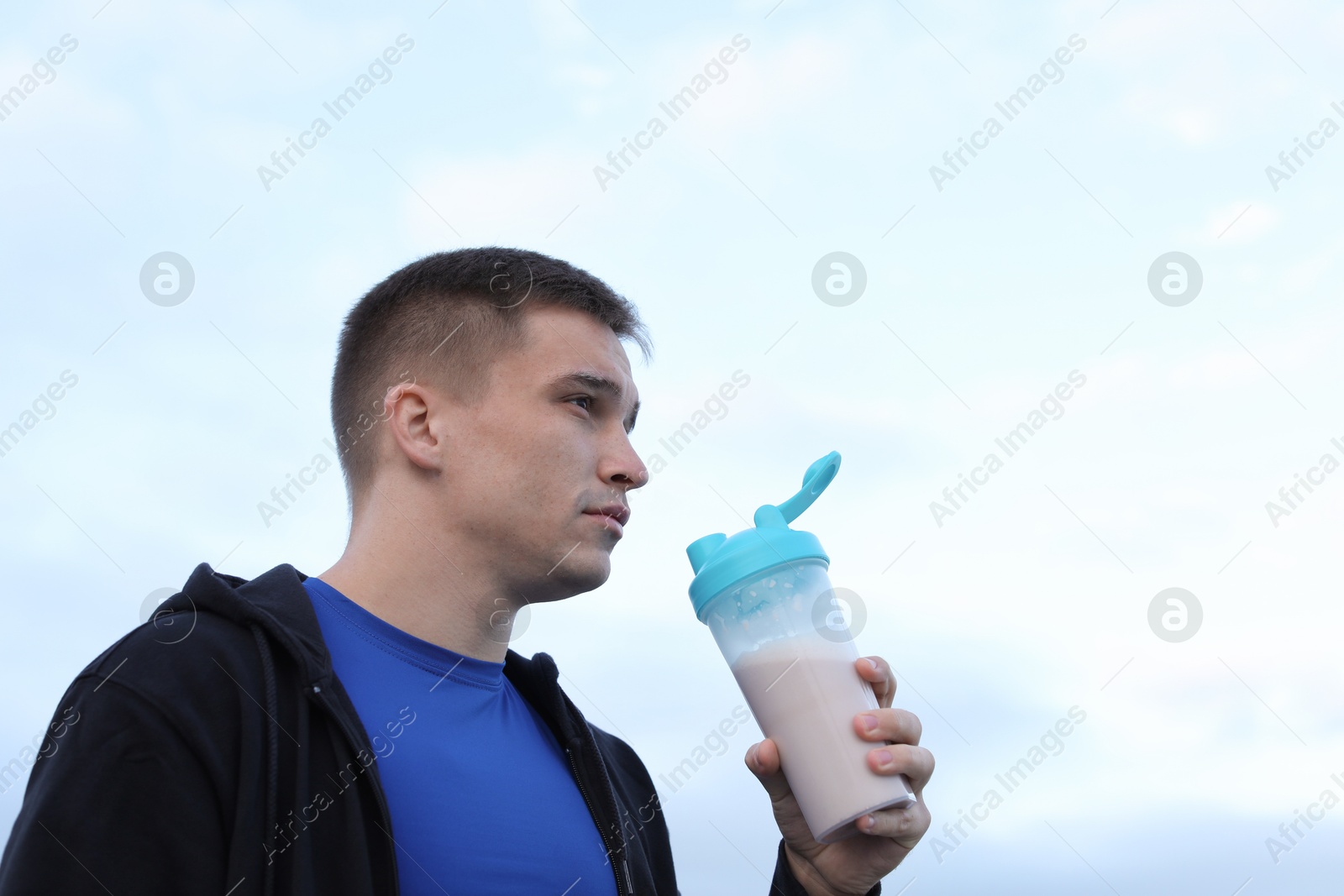 Photo of Athletic man with shaker of protein drink outdoors. Space for text