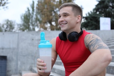 Photo of Smiling man with shaker of protein drink outdoors. Space for text