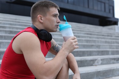 Photo of Handsome athletic man drinking protein shake outdoors. Space for text