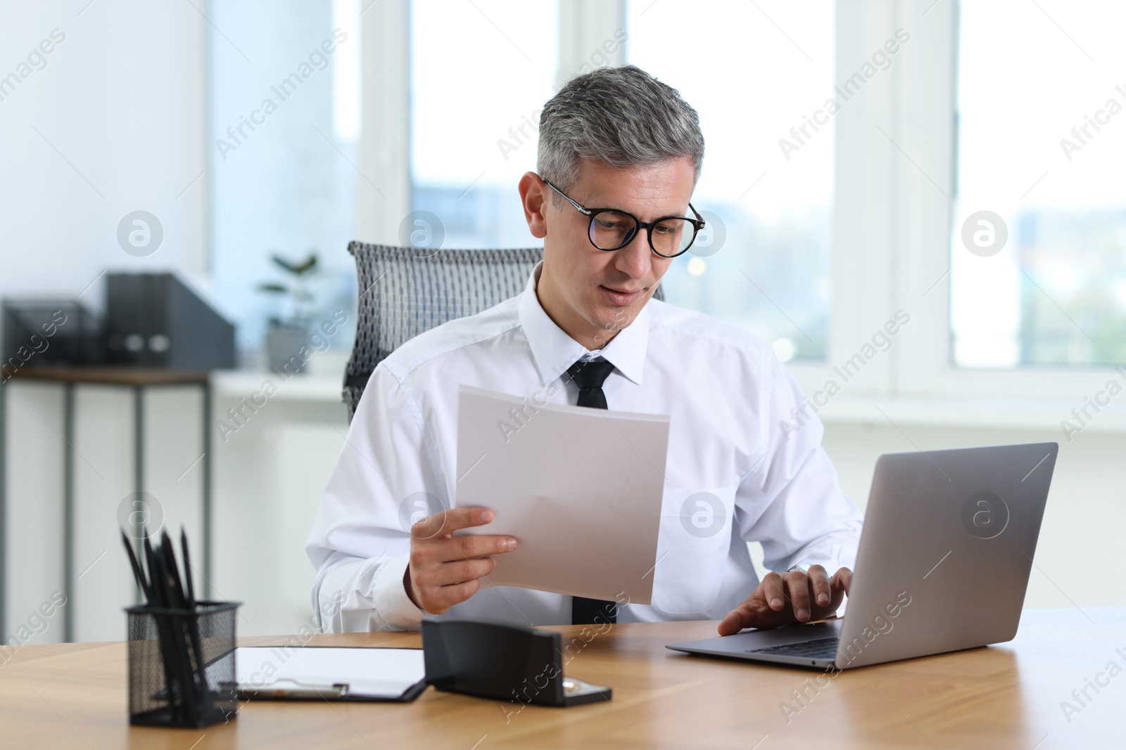 Photo of Businessman with documents working on laptop at table in office