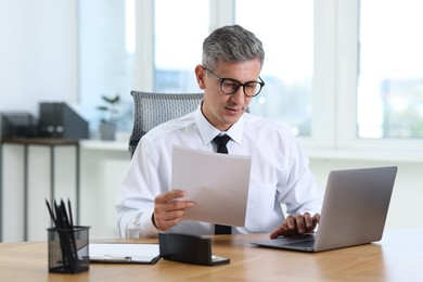 Businessman with documents working on laptop at table in office