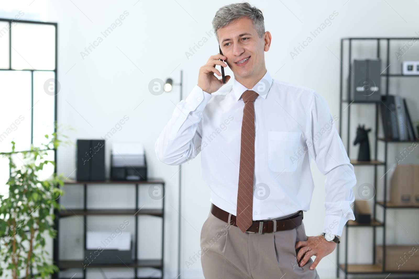 Photo of Happy businessman talking on smartphone in office