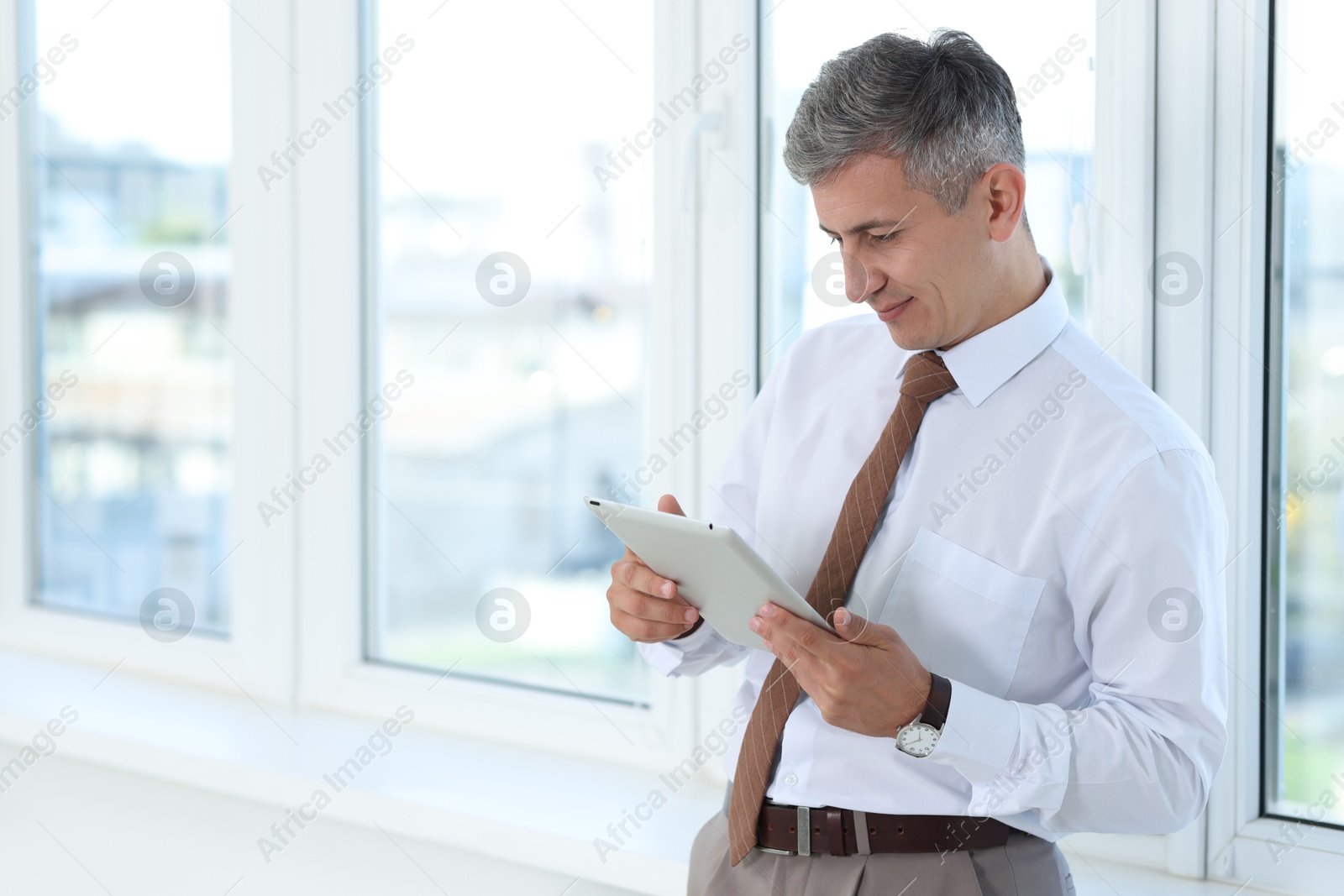 Photo of Businessman using tablet near window in office, space for text