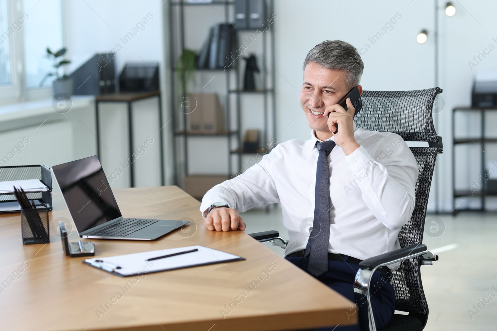 Photo of Businessman talking on smartphone at table in office