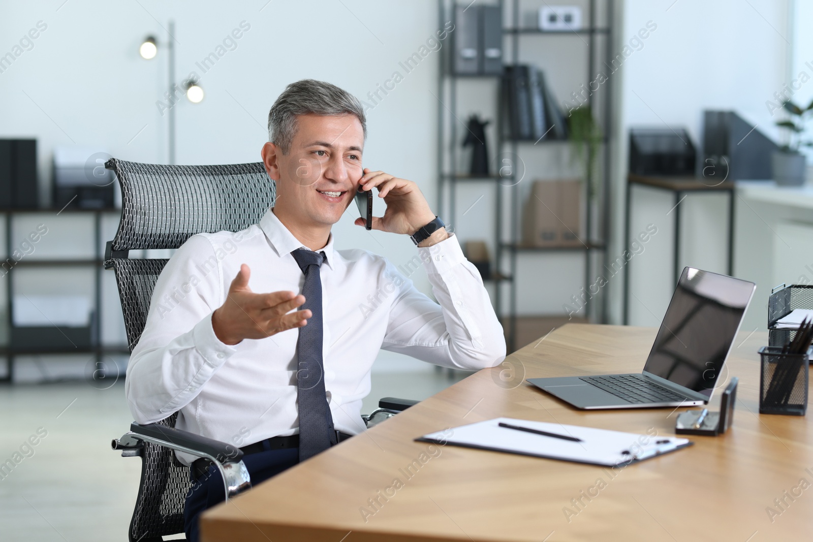 Photo of Businessman talking on smartphone at table in office