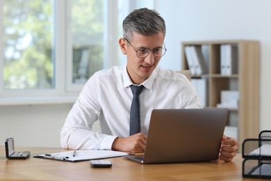 Photo of Businessman working on laptop at table in office