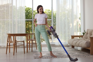 Photo of Smiling young woman cleaning floor with cordless vacuum cleaner at home