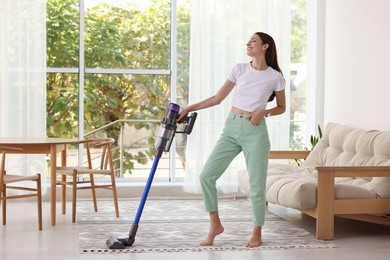 Photo of Smiling young woman cleaning floor with cordless vacuum cleaner at home