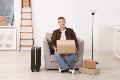 Photo of Happy man with moving boxes and suitcase in new apartment. Housewarming party