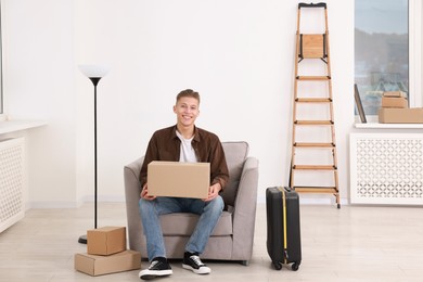 Photo of Happy man with moving boxes and suitcase in new apartment. Housewarming party