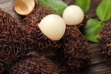 Delicious ripe rambutans and green leaves on wooden table, closeup