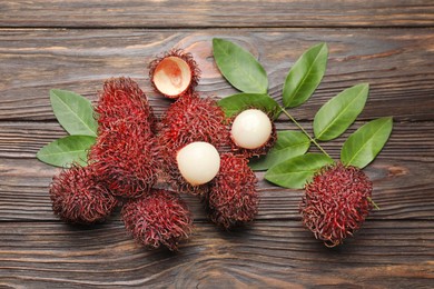 Photo of Delicious ripe rambutans and green leaves on wooden table, flat lay