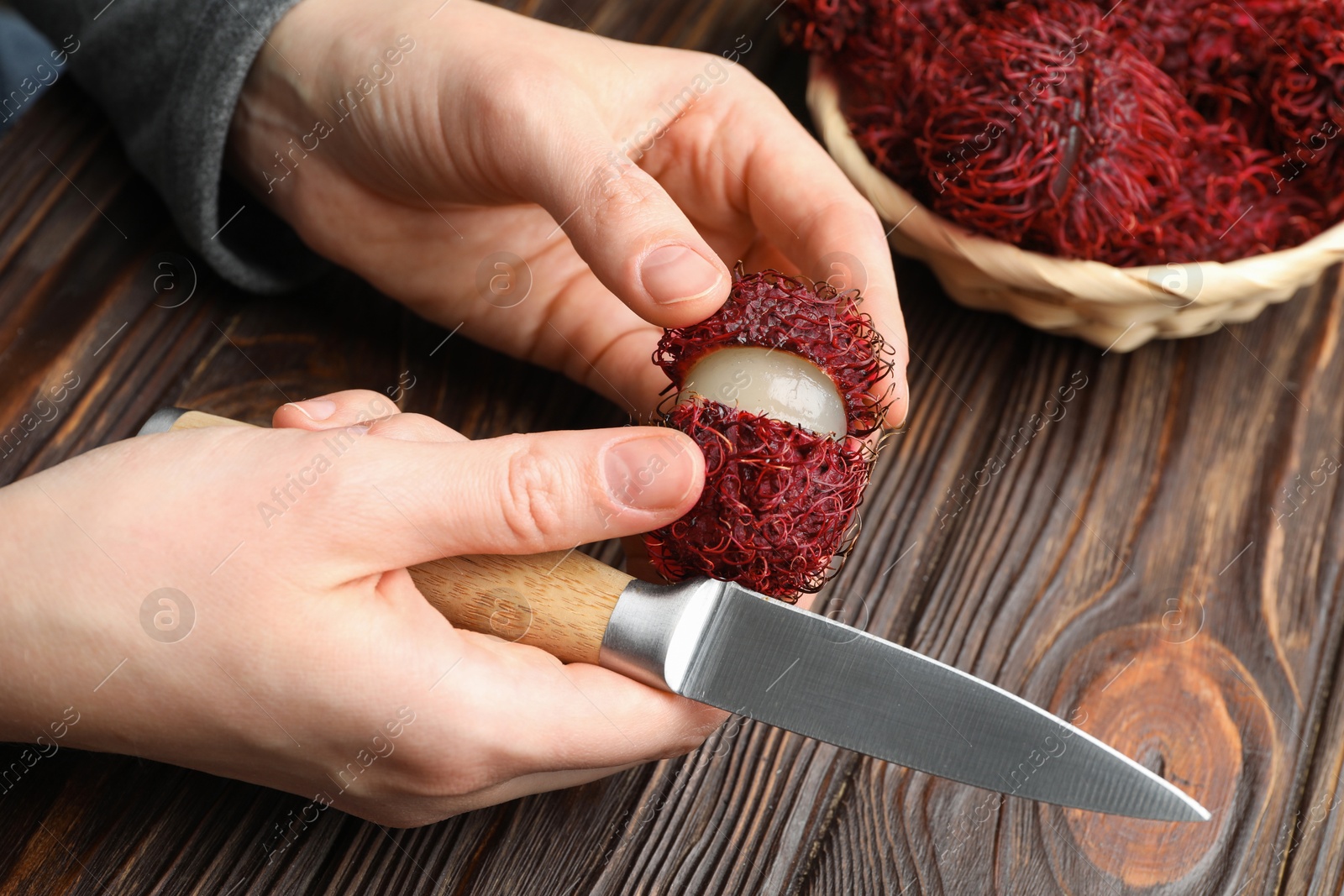 Photo of Woman peeling ripe rambutan at wooden table, closeup