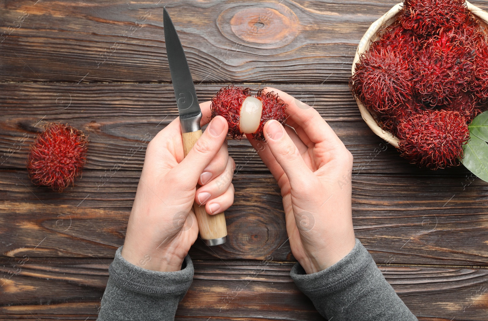 Photo of Woman peeling ripe rambutan at wooden table, top view