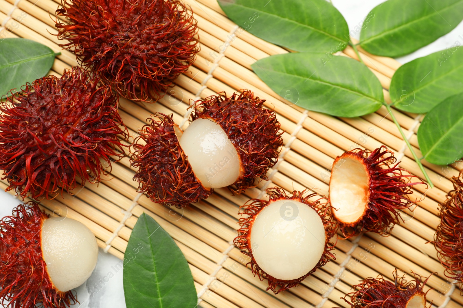 Photo of Delicious ripe rambutans and green leaves on table, flat lay