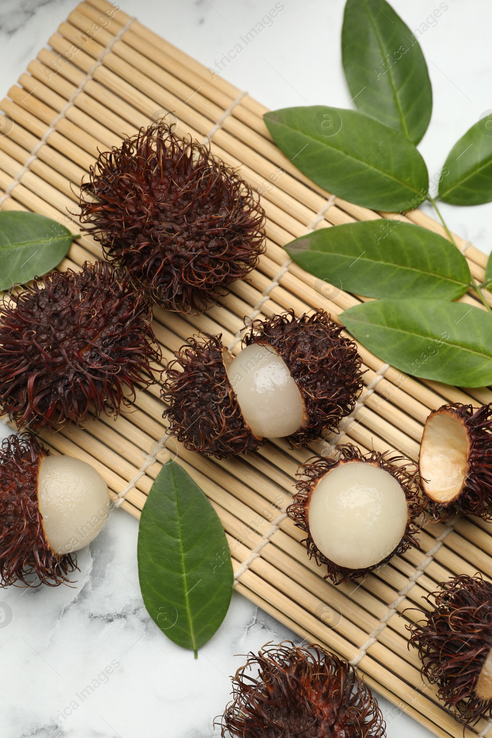 Photo of Delicious ripe rambutans and green leaves on white marble table, flat lay