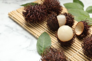 Photo of Delicious ripe rambutans and green leaves on white marble table, closeup. Space for text