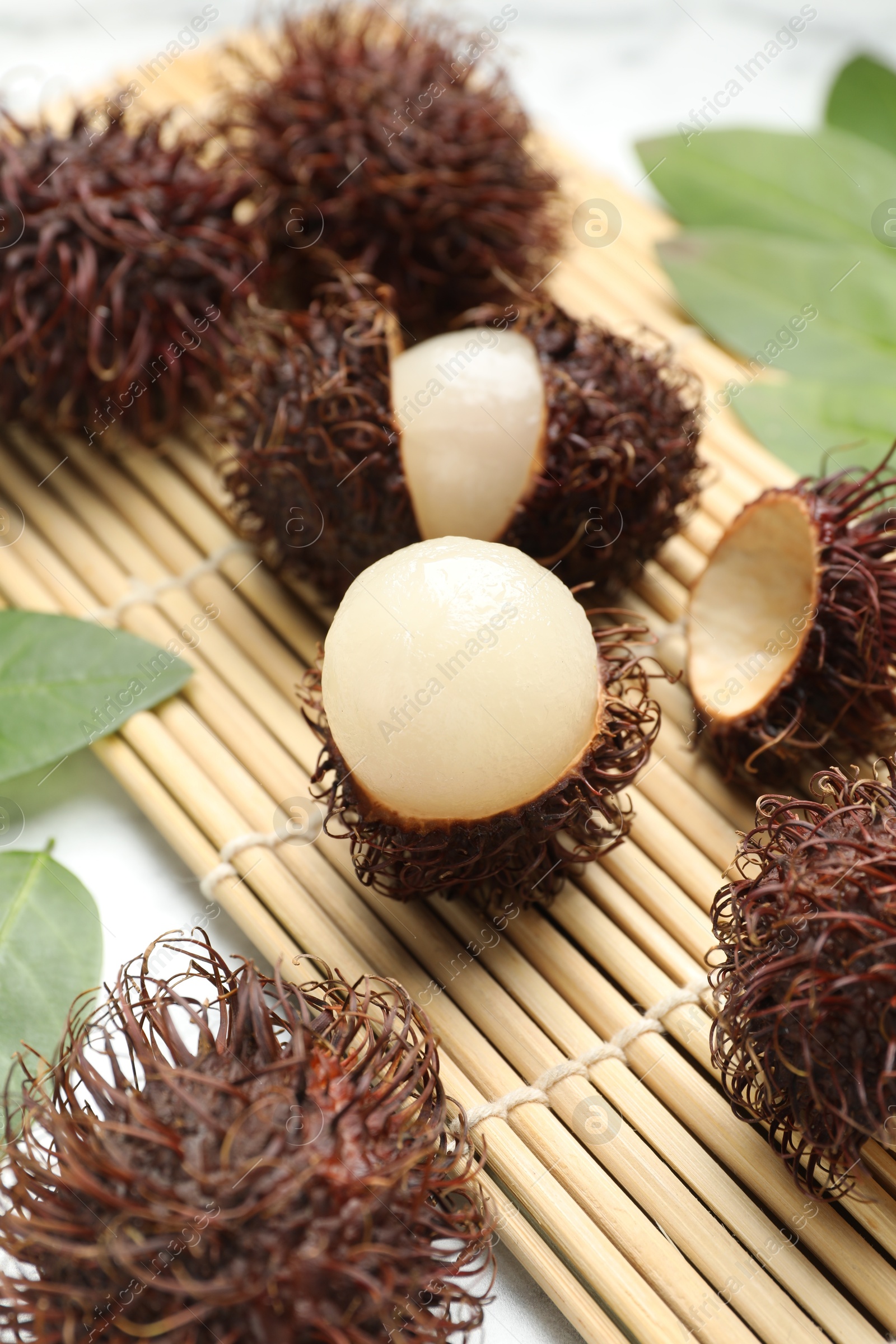 Photo of Delicious ripe rambutans and green leaves on table, closeup