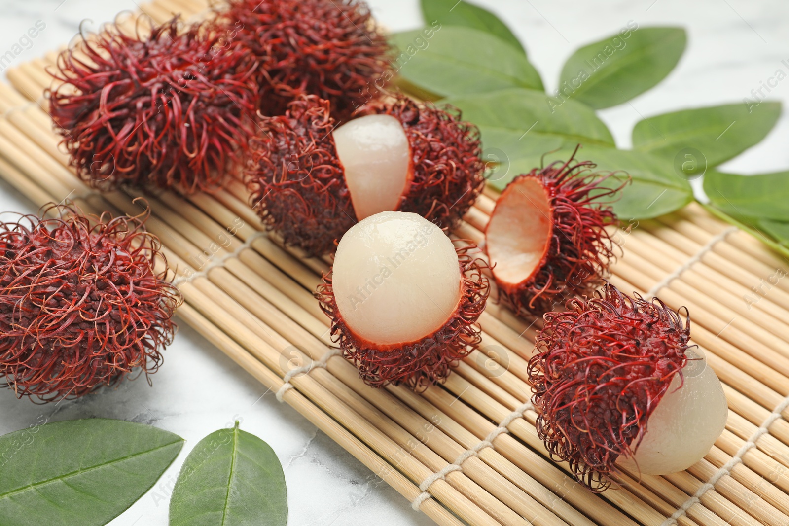 Photo of Delicious ripe rambutans and green leaves on white marble table, closeup