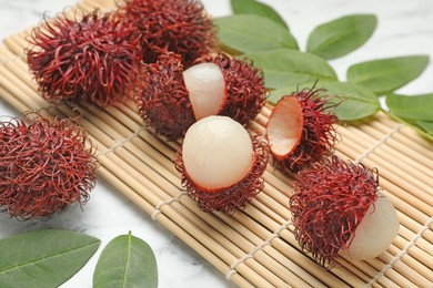 Delicious ripe rambutans and green leaves on white marble table, closeup