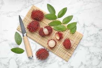 Delicious ripe rambutans, knife and green leaves on white marble table, flat lay