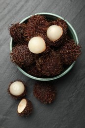 Photo of Delicious ripe rambutans in bowl on black table, top view