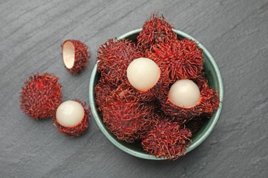 Photo of Delicious ripe rambutans in bowl on black table, top view