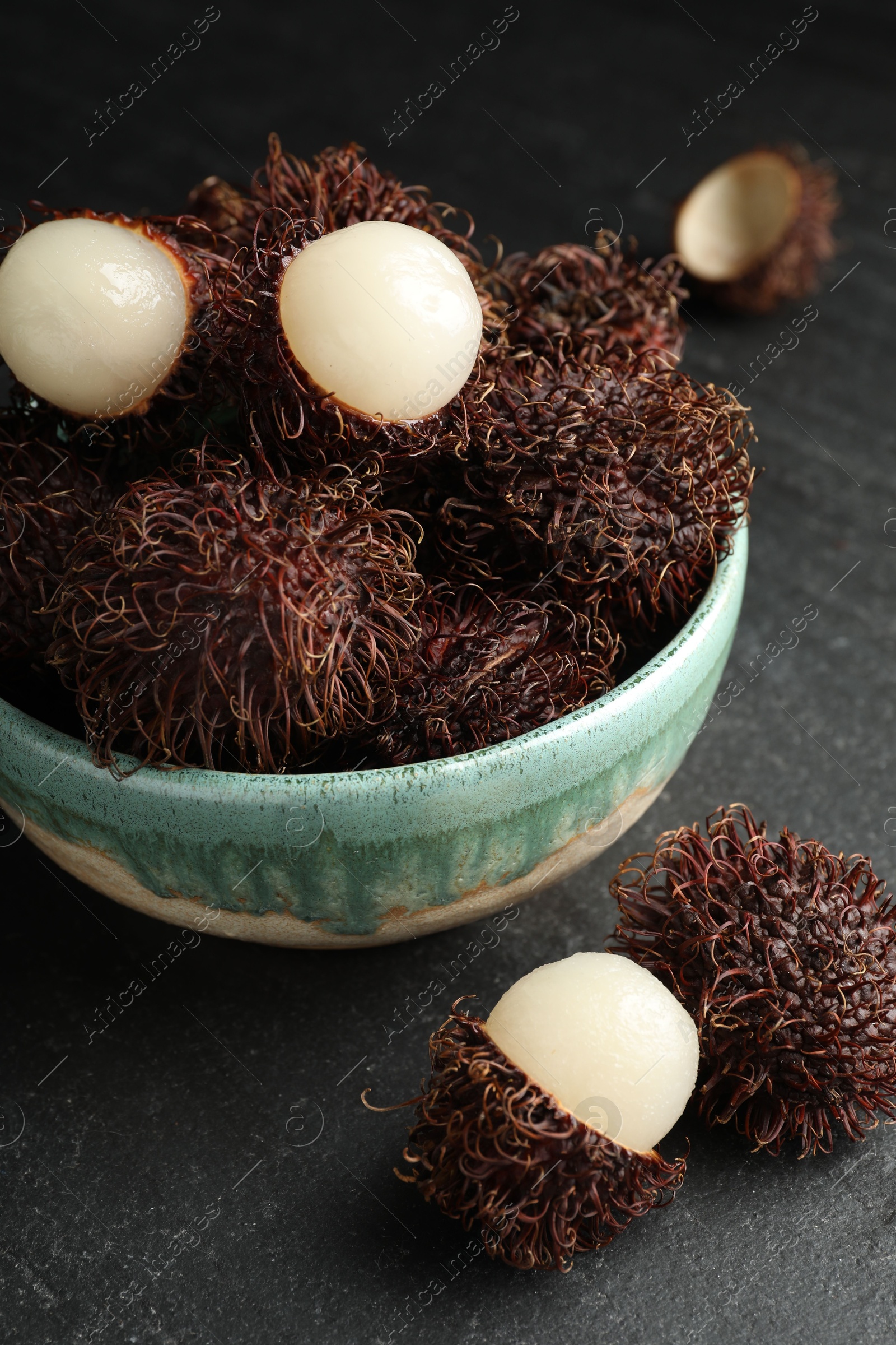 Photo of Delicious ripe rambutans in bowl on black table, closeup