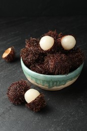 Photo of Delicious ripe rambutans in bowl on black table, closeup