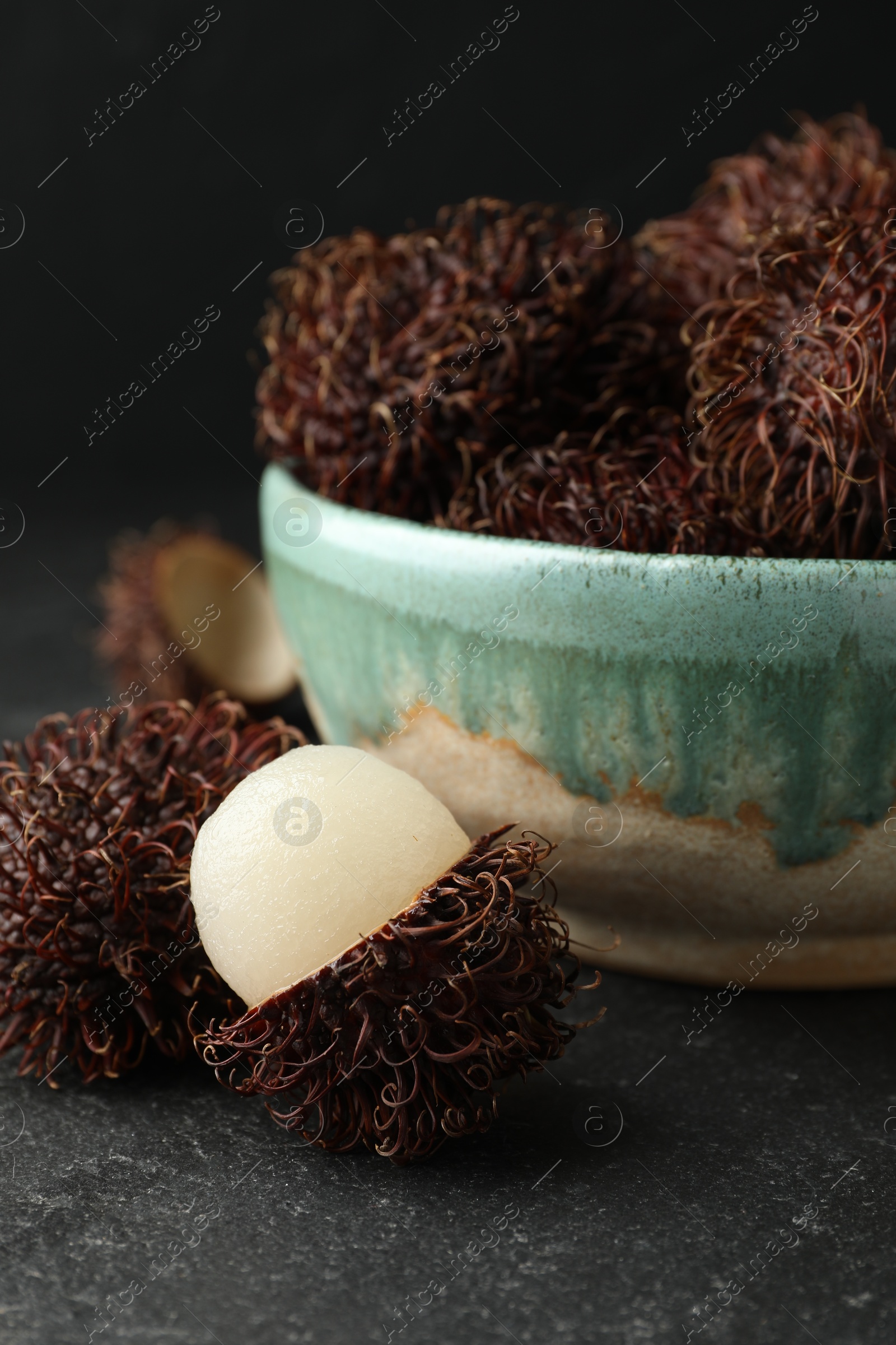 Photo of Delicious ripe rambutans in bowl on black table, closeup