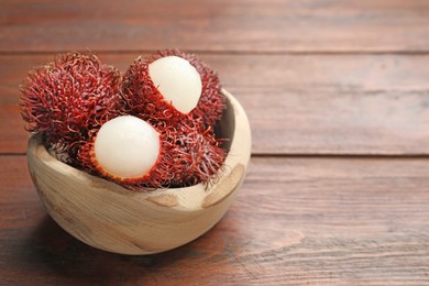 Photo of Delicious ripe rambutans in bowl on wooden table, closeup. Space for text