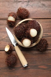 Photo of Delicious ripe rambutans in bowl and knife on wooden table, flat lay