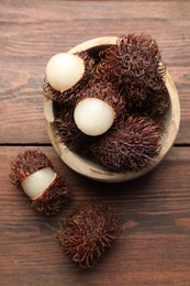 Delicious ripe rambutans in bowl on wooden table, top view